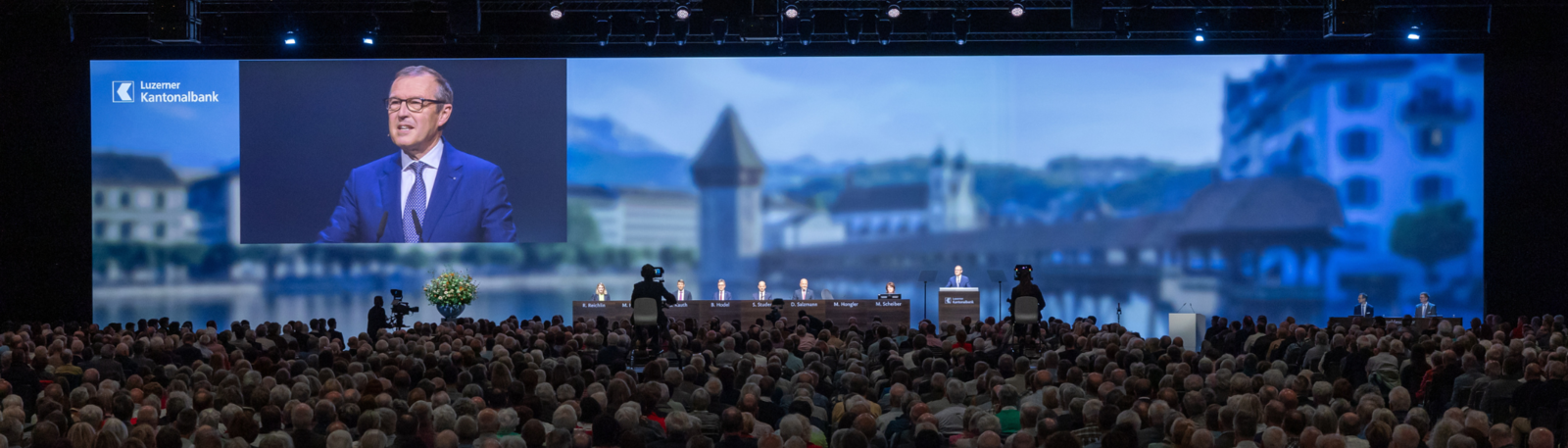 Leinwand und Podim mit Gästen an der GV der LUKB. 