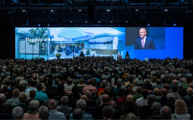 Grosse Leinwand und Podium mit vielen Gästen an der Generalversammlung der Luzerner Kantonalbank.